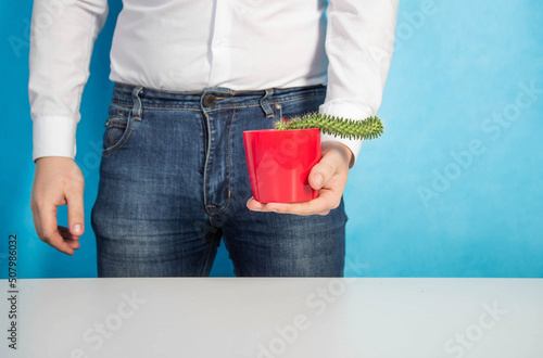 Slika na platnu A man holds a red pot with a cactus against a blue wall