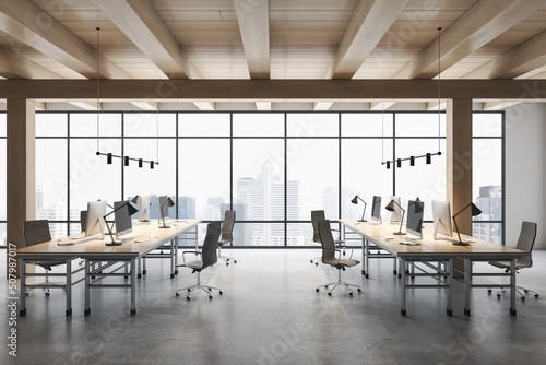 Front view on stylish workspace rows with modern computers on concrete floor in spacious coworking office with wooden ceiling and city view from huge window. 3D rendering photo