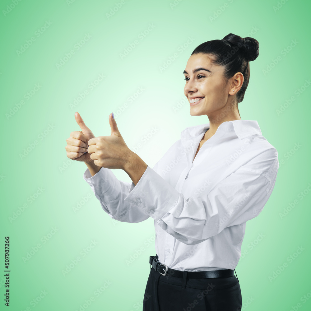 Like concept with happy young businesswoman in white shirt holding thumbs up on light green background, close up, isolated Like concept with happy young businesswoman in white shirt holding thumbs up on light green background, close up, isolated