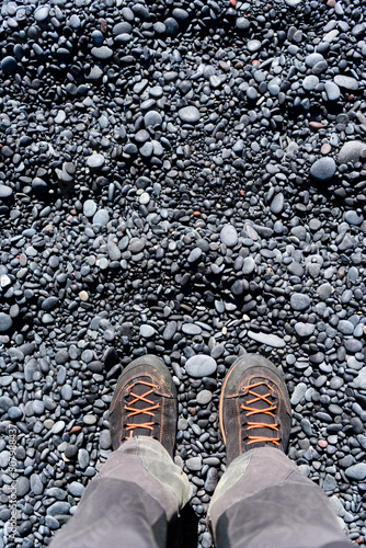 Legs in grey hinking trousers and black orange hiking boots on black pebbles photo