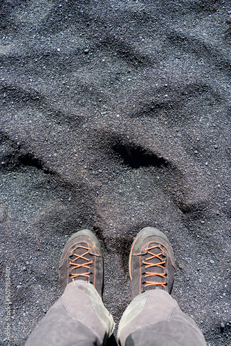 Legs in grey hinking trousers and black orange hiking boots on black sand photo