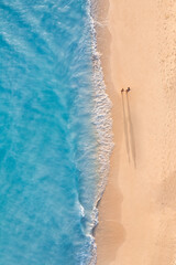 Aerial view of couple walking on beach with sunlight close to turquoise sea waves. Top view of summer beach landscape, romantic inspirational couple vacation, romance holiday. Freedom travel template