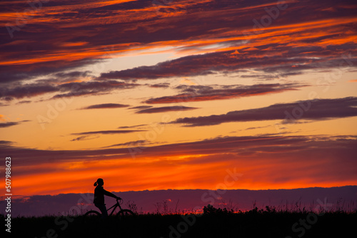 women riding bike at sunset. girls on a bike at beautiful sunset sky. silhouette of cyclist.