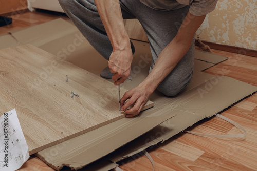 High angle of crop man assembling wooden furniture with screwdriver on floor at home  photo