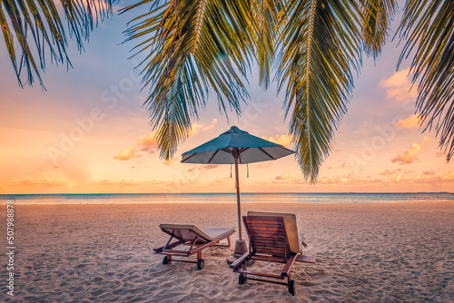 Beautiful tropical sunset  two sun beds  loungers  umbrella under palm tree. Fantastic colorful sky sand  sea view calm relax landscape. Beach resort landscape. Romantic love couple travel template