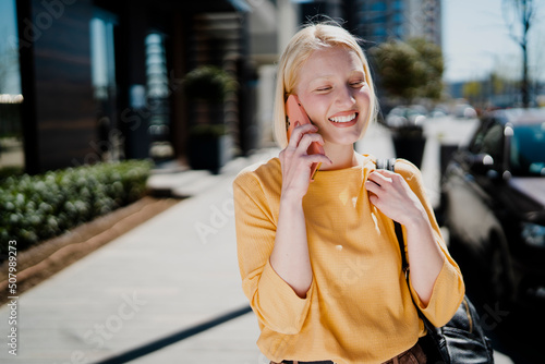 Happy girl walking on the street using the phone. Beautiful blonde girl talking to the smartphone..