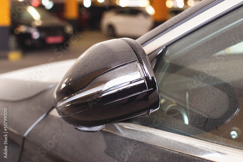 Modern folding car mirror with turn signal. Black car, close-up.