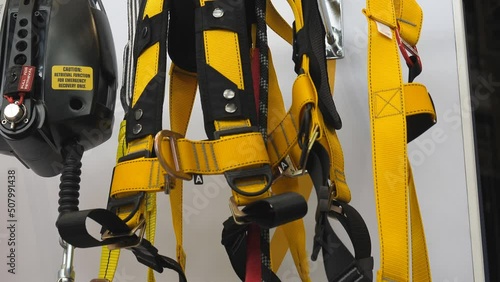 Tilt down shot showing fall arrest harness hanging against white wall background.
