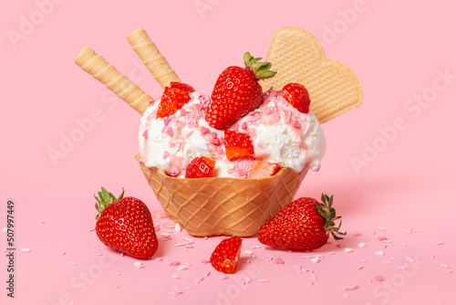 cone with scoops of ice cream strewed sprinkles, poured with glaze and decorated strawberries on pink background
