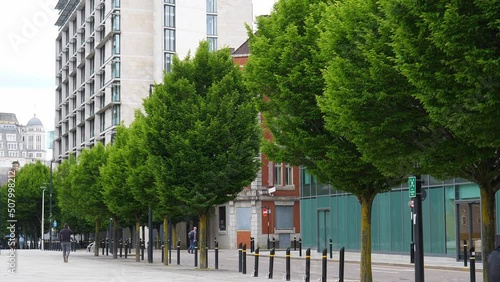 Rear view of people walking past nice green tree line in pedestrian area in Manchester city centre. photo