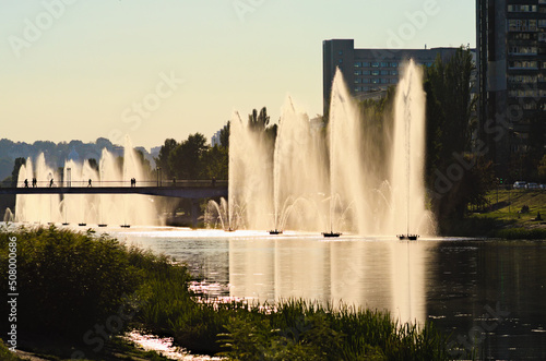 Beautiful sunset landscape of Rusanivka neighborhood at sunny day. Fountains in the city channel. Green hills of the right bank of the Dnieper River in the background. Autumn season landscape