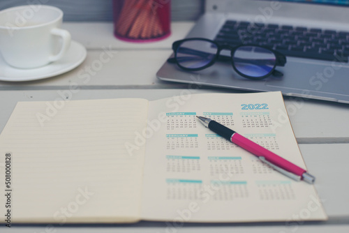 Planner write meeting agenda at Calendar book, work online at home. Diary for organizer to plan timetable, daily appointment, and management job at office desk. Planner book and 2022 Calendar Concept.
