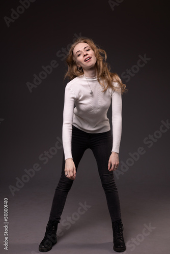 Portrait of playful girl making faces. Mixed emotions on face: fooling, flirting and smiling. Sitting, black background.