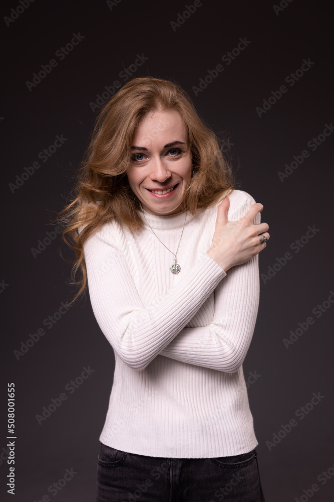 Happy young girl with long blond hair smiling. Young woman in white sweater pleased and satisfied. Portrait of emotional lady isolated Happy young girl with long blond hair smiling. Young woman in white sweater pleased and satisfied. Portrait of emotional lady isolated
