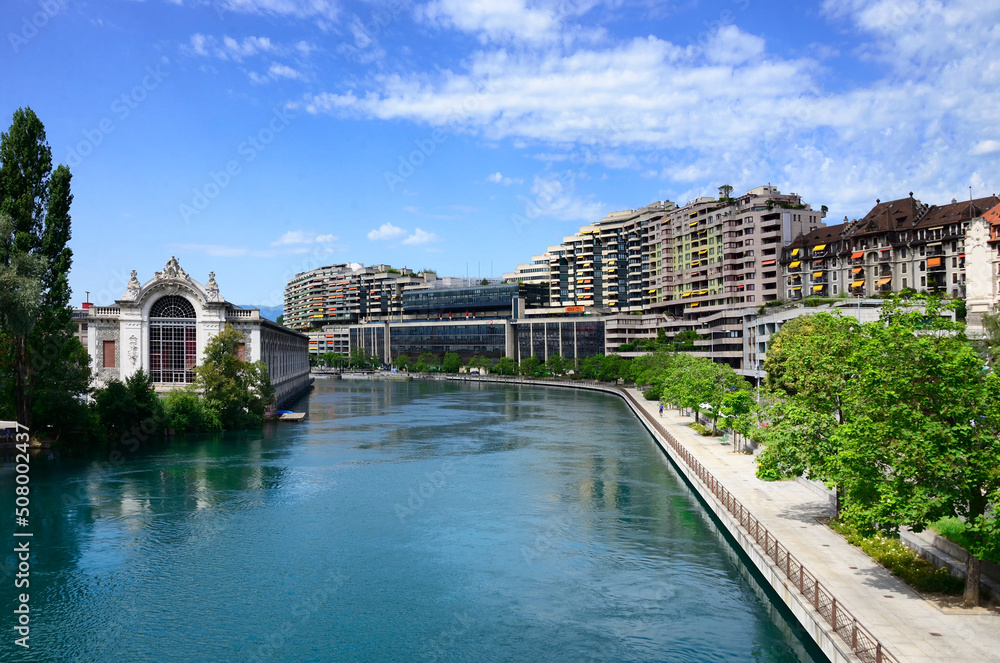 Quai du Seujet along Rhone river, on left historic building of BFM - former hydroelectric power station now a theatre, in background hydropower dam on Rhone river, Geneva, Switzerland, Europe