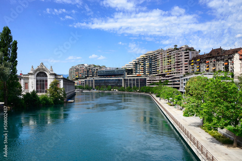 Quai du Seujet along Rhone river, on left historic building of BFM - former hydroelectric power station now a theatre, in background hydropower dam on Rhone river, Geneva, Switzerland, Europe