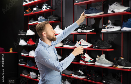 Man choosing sports shoes for running standing in the modern sportswear shop, shopper choosing sports sneakers