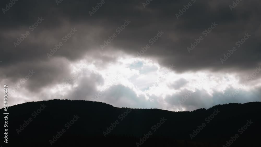 Heavy gray storm clouds in the sky, through which the sun's rays break through. Black mountains. Horizon line. The concept of anxiety, restlessness, sadness Heavy gray storm clouds in the sky, through which the sun's rays break through. Black mountains. Horizon line. The concept of anxiety, restlessness, sadness