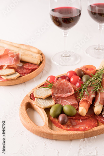 Charcuterie plate with different types of meat snacks - proscuitto. Wooden plates with traditional italian antipasti served with glasses of red wine on white concrete table. Vertical image