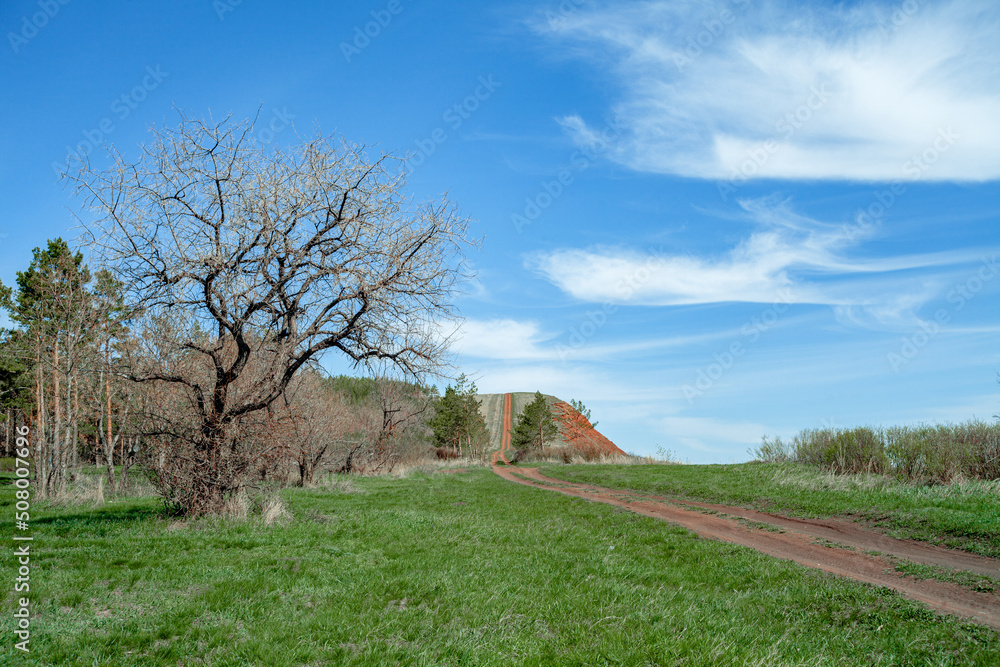 Beautiful landscape on a sunny day. An earthen road. A landscape with a colorful sky under the sun. Mountain slope. Green trees. natural background. Creative image.