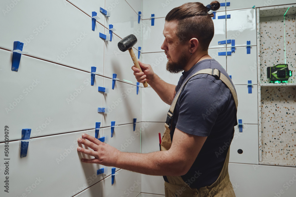 Tiler knocks the wedges of the ceramic tile leveling system off the wall in the bathroom Tiler knocks the wedges of the ceramic tile leveling system off the wall in the bathroom