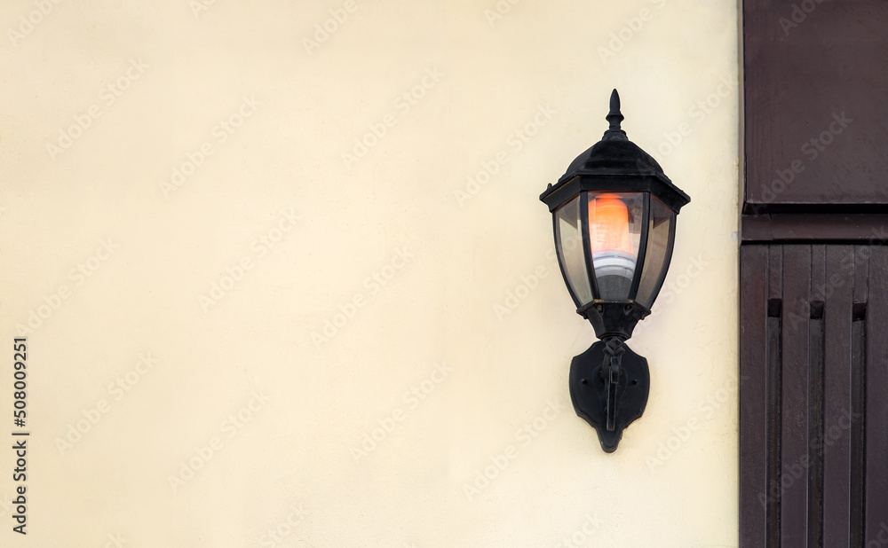 iron wall lantern in retro style in black color with a glass shade and electric light bulb glow with warm light, urban wall lighting on the facade surface of the building with copy space, nobody.