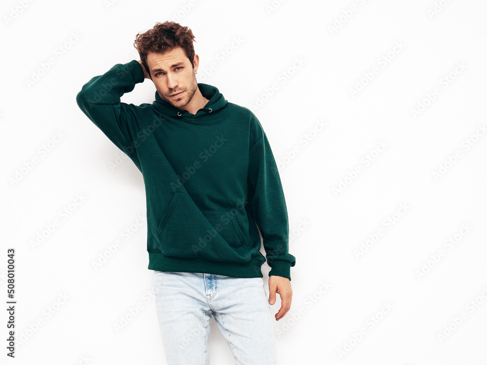 Handsome confident hipster model.Sexy unshaven man dressed in summer stylish green hoodie and jeans clothes. Fashion male with curly hairstyle posing in studio. Isolated on white Handsome confident hipster model.Sexy unshaven man dressed in summer stylish green hoodie and jeans clothes. Fashion male with curly hairstyle posing in studio. Isolated on white