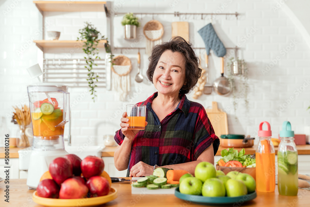 Mature smiling woman cook salad, fruits and vegetables. Attractive mature woman with fresh green fruit salad at home. Senior woman apron standing in the kitchen counter relaxing in house weekend time