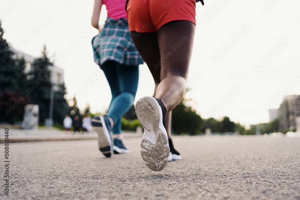 Back view of friends legs in sportswear running in the city. Multiethnic women having a fitness workout. Back view of friends legs in sportswear running in the city. Multiethnic women having a fitness workout.