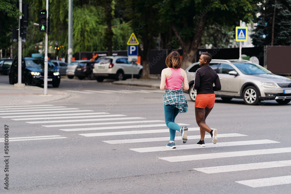 Friends in sportswear running in the city dicussing on pedestrian street. Multiethnic women having a fitness workout.
