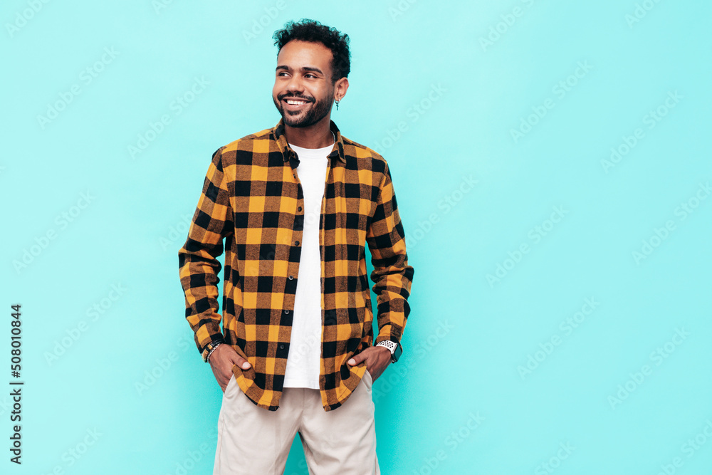 Handsome smiling hipster model. Sexy unshaven man dressed in yellow summer shirt and jeans clothes. Fashion male posing near blue wall in studio. Cheerful and happy. Isolated Handsome smiling hipster model. Sexy unshaven man dressed in yellow summer shirt and jeans clothes. Fashion male posing near blue wall in studio. Cheerful and happy. Isolated