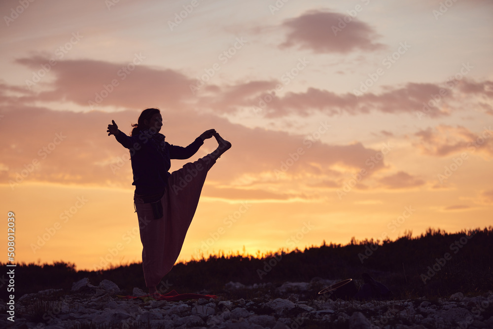 Fototapeta premium Woman practicing yoga outdoors in sunset sunrise time.