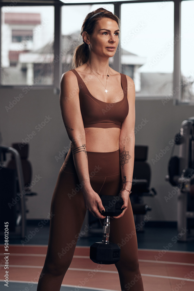 Pretty woman working out in a gym with small weights. Adult lady with beautiful shaped body.
