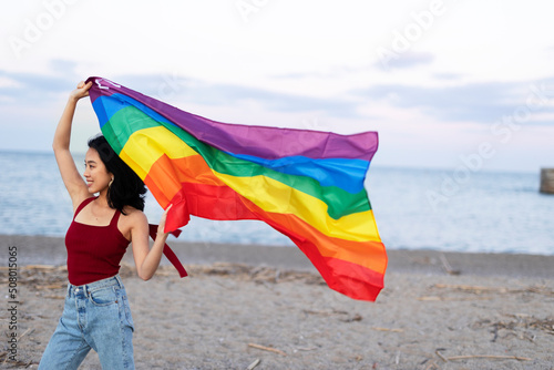 Happy girl with a pride flag at the beach. LGBT community.