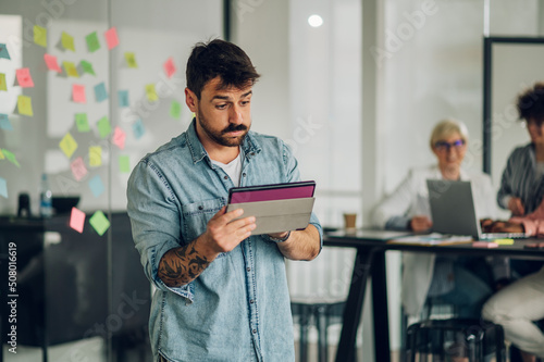 Business man using tablet in the office with his team working in the back