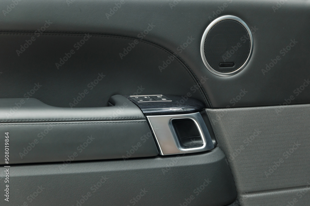 The concept of detailing. Black leather car door panel. Chrome door handle. The interior of the car. Interior trim of the car door, speaker, door lock control unit and door handle. Close-up.