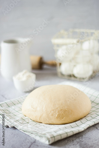 A ball of dough on a white rustic table with flour and a napkin. Homemade dough for pizza or bread.