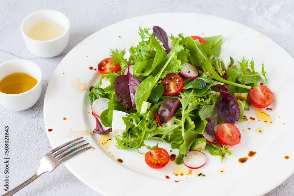 Green salad of fresh lettuce leaves, cherry tomatoes, feta cheese and assorted seeds with a sauce of honey, olive oil and balsamic vinegar on a flat plate on a stone table. Healthy vegan food. Green salad of fresh lettuce leaves, cherry tomatoes, feta cheese and assorted seeds with a sauce of honey, olive oil and balsamic vinegar on a flat plate on a stone table. Healthy vegan food.