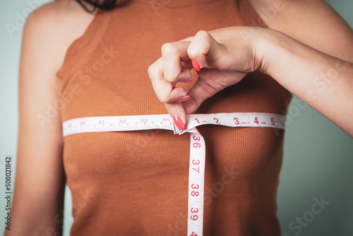Slim woman measures her breast with a measuring tape
