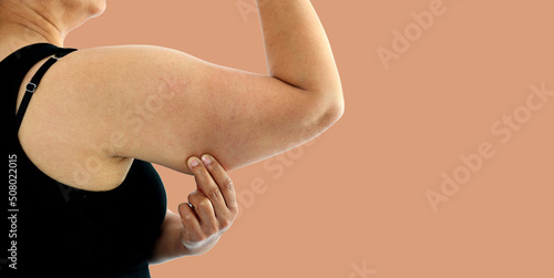 A young Asian woman grabbing skin on her upper arm with excess fat isolated on a white background. Pinching the loose and saggy muscles. Overweight concept