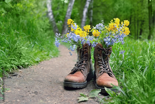 bouquet of wild flowers in old leather shoes on village road close up, green natural background. spring summer season. beautiful floral composition