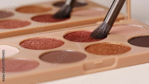 Make-up artist takes eyeshadows from cosmetic eyeshadow palette using brush.