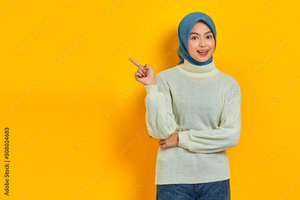 Shocked beautiful Asian woman in white sweater pointing fingers aside at copy space isolated over yellow background Shocked beautiful Asian woman in white sweater pointing fingers aside at copy space isolated over yellow background