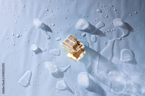 Foto Golden mirror rubik's cube, pieces of melted ice on a blue background with water drops
