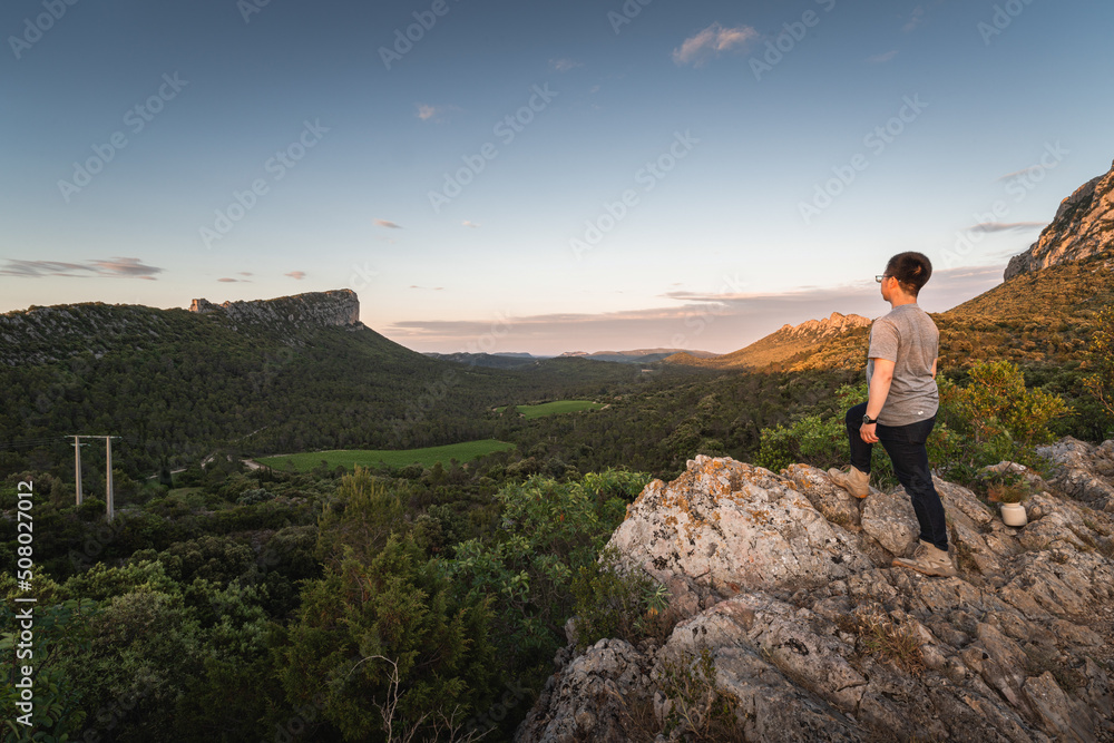 A man standing on the cliff edge, looking over the Pic Saint-Loup and Pic de l'Hortus, two famous mountains in the south Fance