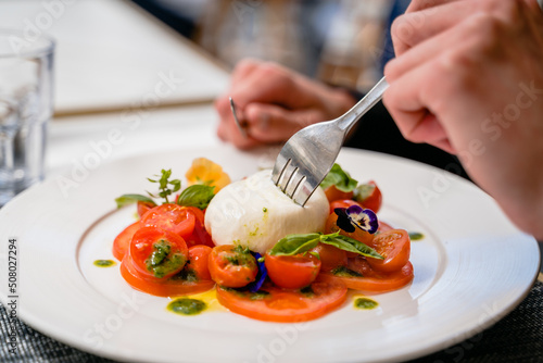 Une personne plante une fourchette dans une mozzarella avec des tomates et du basilic dans un restaurant  photo