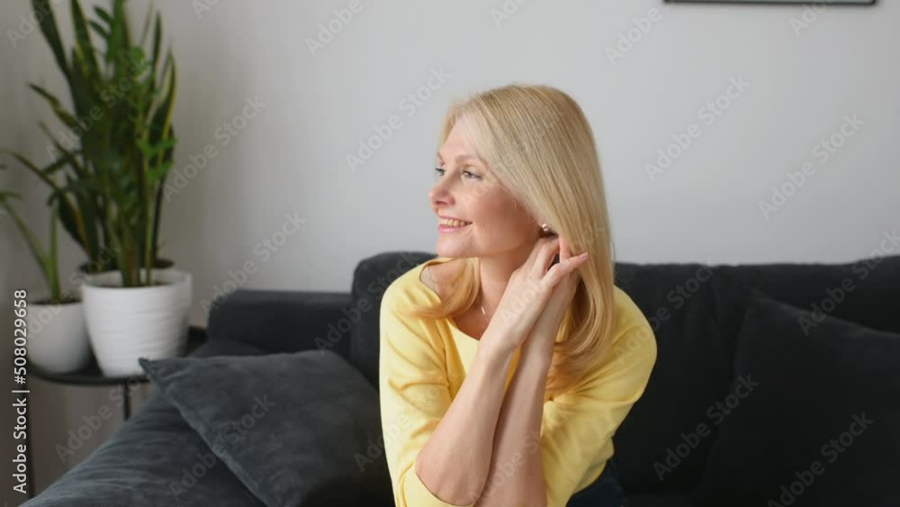 Full length view of the winsome senior lady is resting near the comfortable couch at home. Charming elderly woman in casual wear smiling and daydreaming in relaxed atmosphere. Wellbeing concept Full length view of the winsome senior lady is resting near the comfortable couch at home. Charming elderly woman in casual wear smiling and daydreaming in relaxed atmosphere. Wellbeing concept