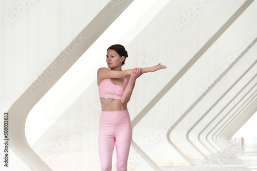 Woman doing an arm stretch exercise, warming up. Urban setting.