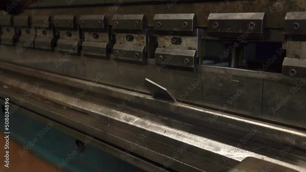 Man working with sheet metal on CNC hydraulic press brake. He puts the part and bends it into a large machine at an angle. Flat footage Man working with sheet metal on CNC hydraulic press brake. He puts the part and bends it into a large machine at an angle. Flat footage