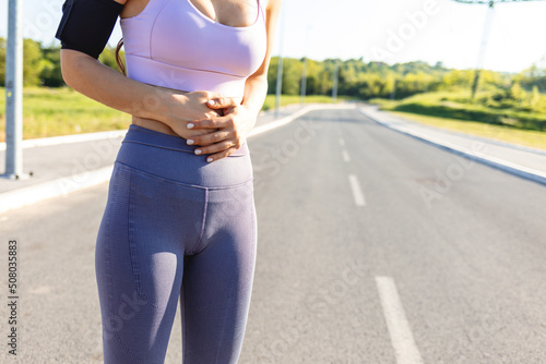 Young sport woman having pain at her stomach. Sports woman with hands on her belly having stomach related issues. Health problem concept.